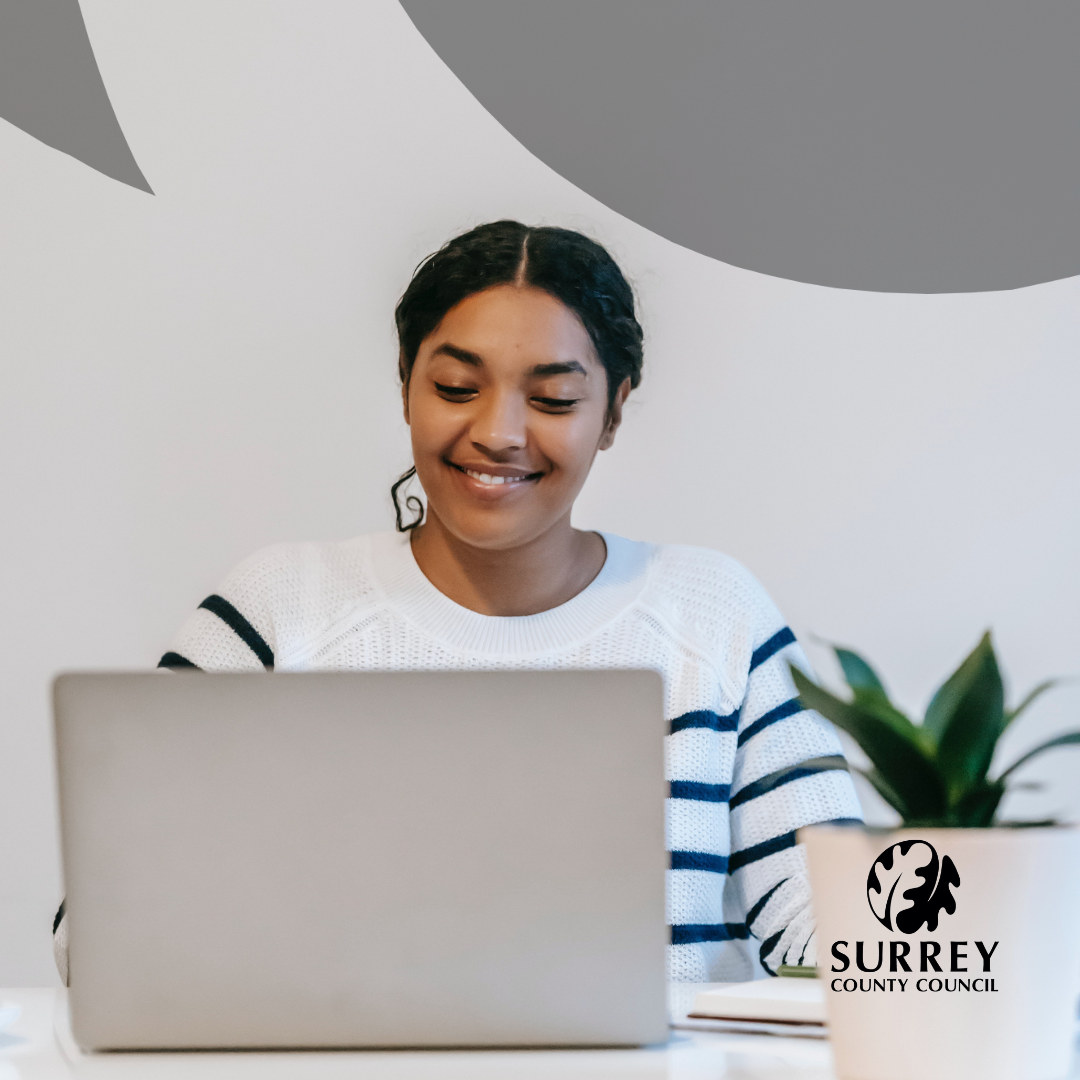 An image of a lady, smiling, using a laptop. Surrey County Council logo.
